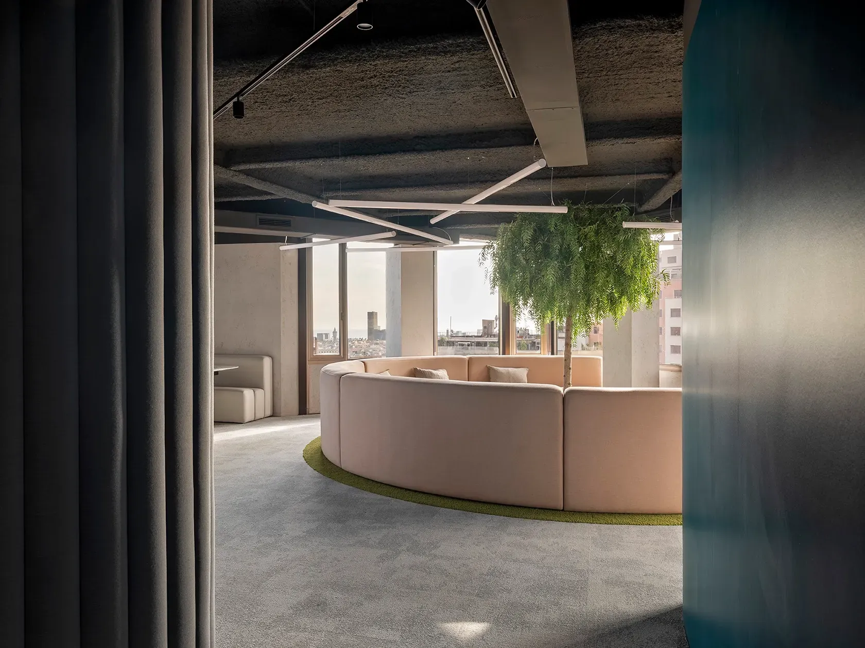 Curved lounge seating area with central tree and panoramic city views in luxury workspace by LUV Studio.