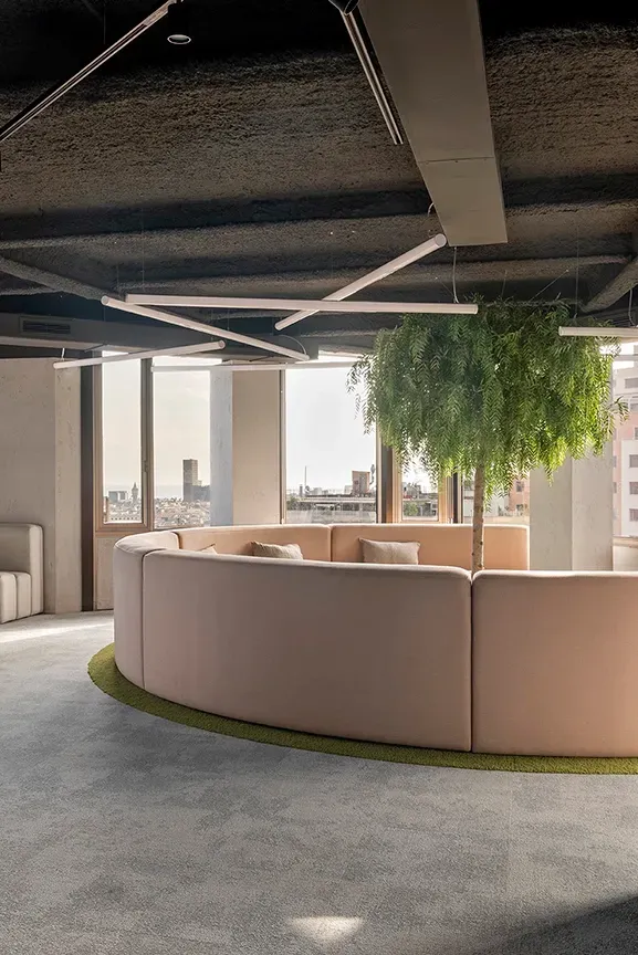 Curved lounge seating area with central tree and panoramic city views in luxury workspace by LUV Studio.