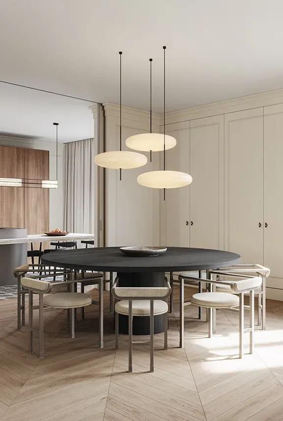 Elegant dining area with a large round black table, cream walls, soft drapes, and pendant lighting.