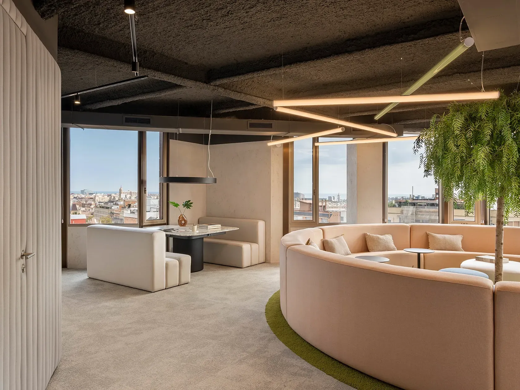 Workspace with meeting booths and a circular lounge under architectural ceiling lights, by LUV Studio.