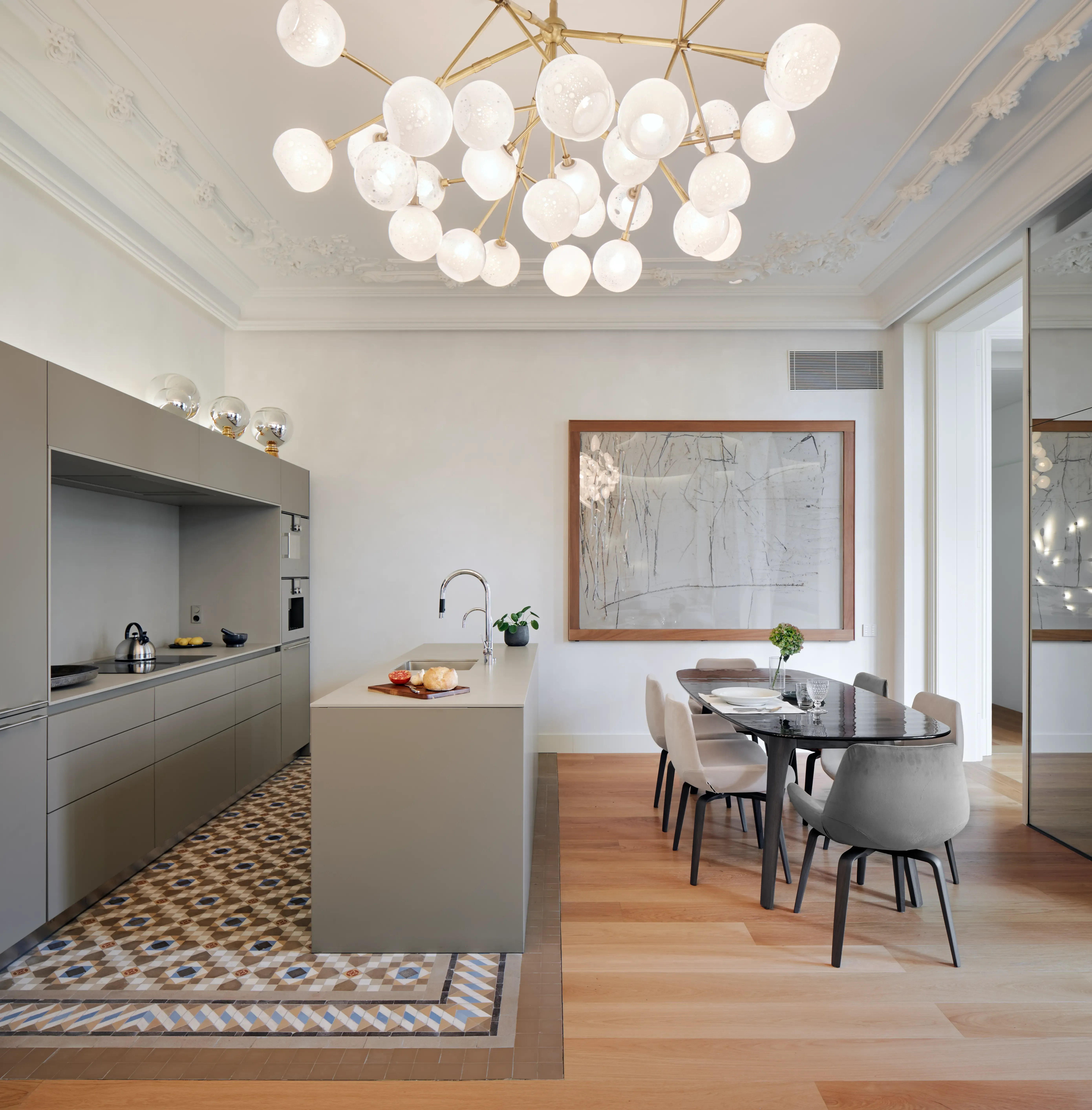 Contemporary open-plan kitchen and dining area with sleek cabinetry, marble-top table, and striking chandelier enhancing refined apartment design.