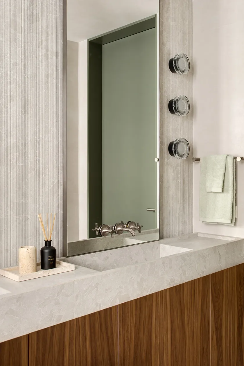 Bathroom vanity in light grey stone with integrated double sink, walnut wood cabinetry and vertical textured wall tiles.