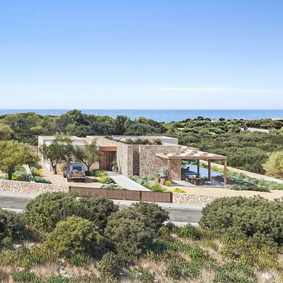 Aerial view of a luxury seaside villa with minimalist architecture, surrounded by Mediterranean landscape.