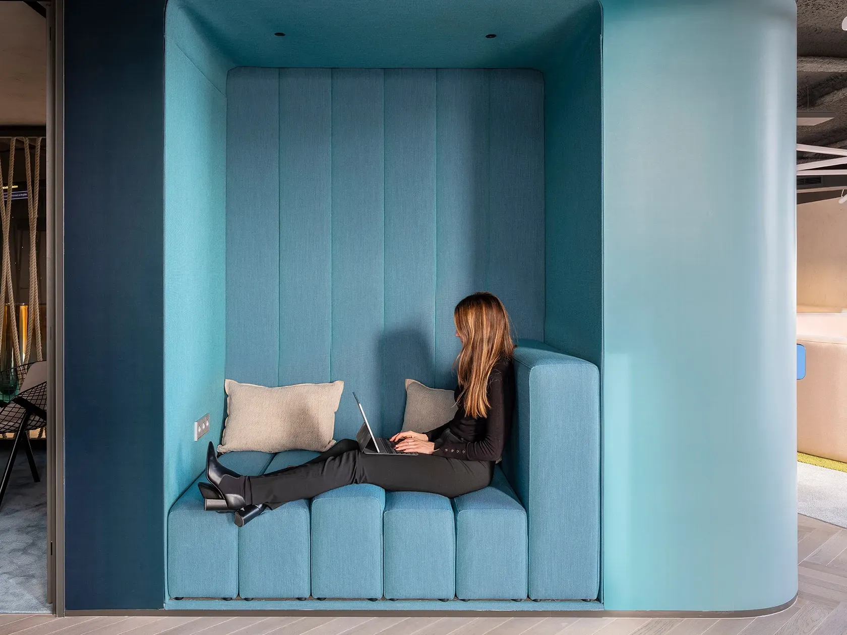 Blue upholstered niche with built-in bench and laptop work setup at LUV Studio’s Urquinaona Office