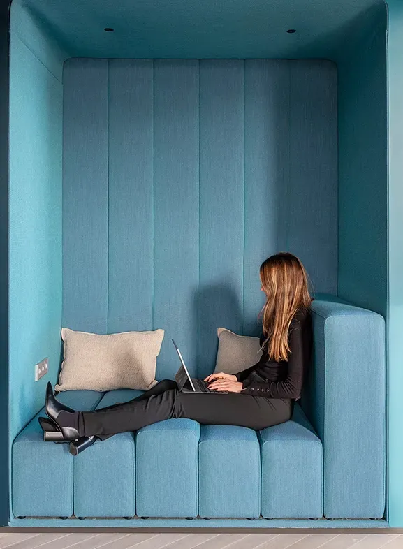 Blue upholstered niche with built-in bench and laptop work setup at LUV Studio’s Urquinaona Office