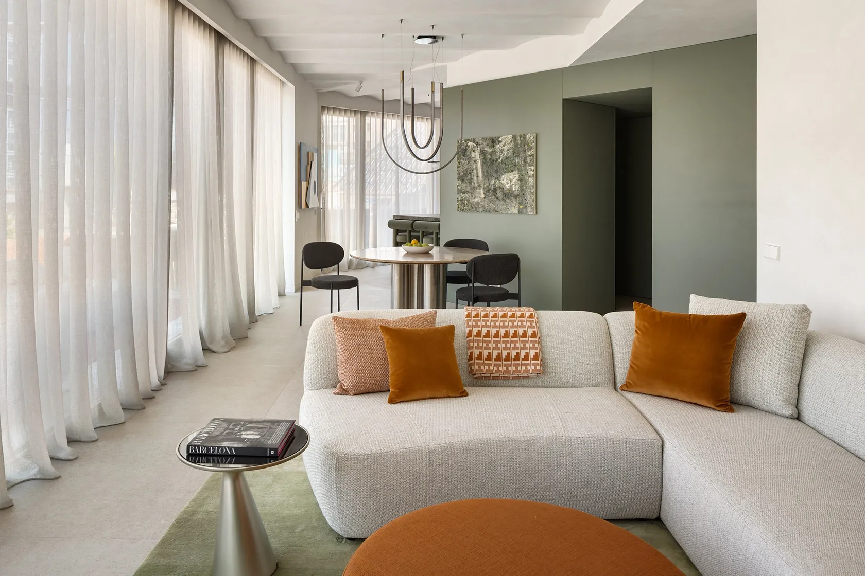 Open living area with light grey modular sofa, terracotta cushions, round ottoman and green area rug next to dining zone.