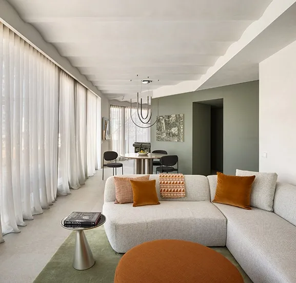 Open living area with light grey modular sofa, terracotta cushions, round ottoman and green area rug next to dining zone.