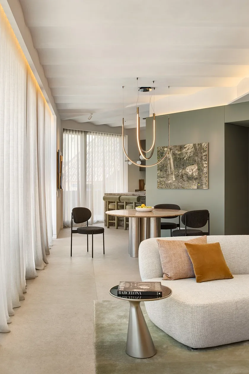 Living and dining space with floor-to-ceiling sheer curtains, curved sofa, accent cushions and statement pendant light.