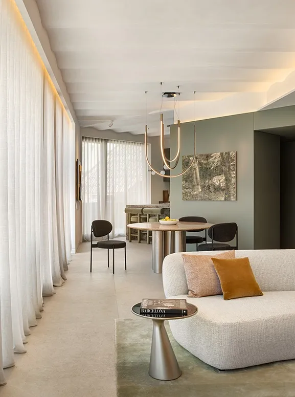 Living and dining space with floor-to-ceiling sheer curtains, curved sofa, accent cushions and statement pendant light.