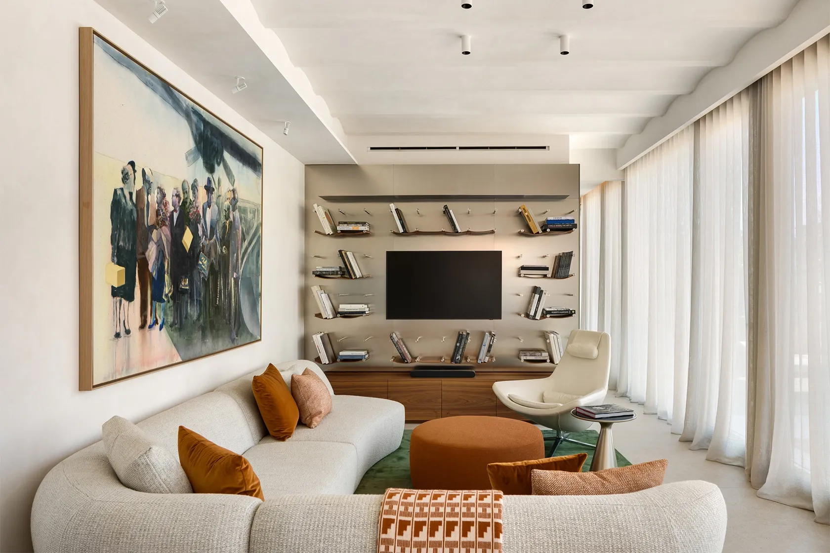 Curved sectional sofa with warm-toned cushions facing large artwork and integrated metal bookshelf with TV.
