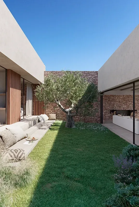 Courtyard with central olive tree at luxury villa by LUV Studio, surrounded by natural stone walls and large glass doors.