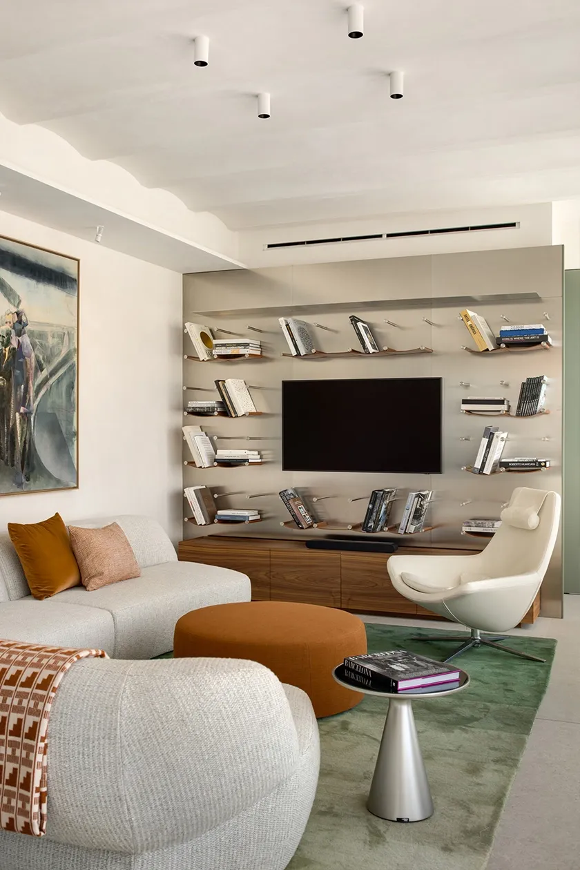 Contemporary living space with modular sofa, leather lounge chair, round ottoman and floating metal bookshelves as TV feature wall.