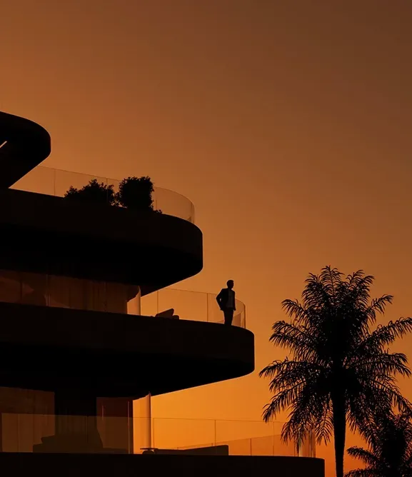 Silhouette of a person standing on a terrace at sunset with palm trees in the background.