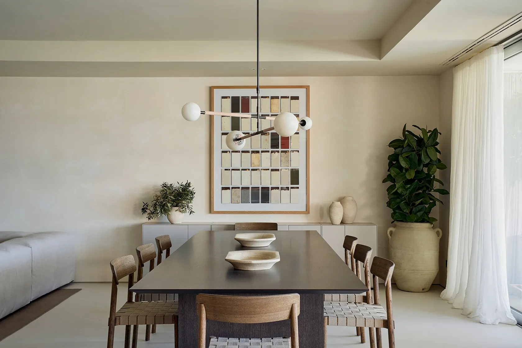 Dining room with wooden table, woven chairs, and modern pendant lamp, blending natural materials in a Mediterranean retreat