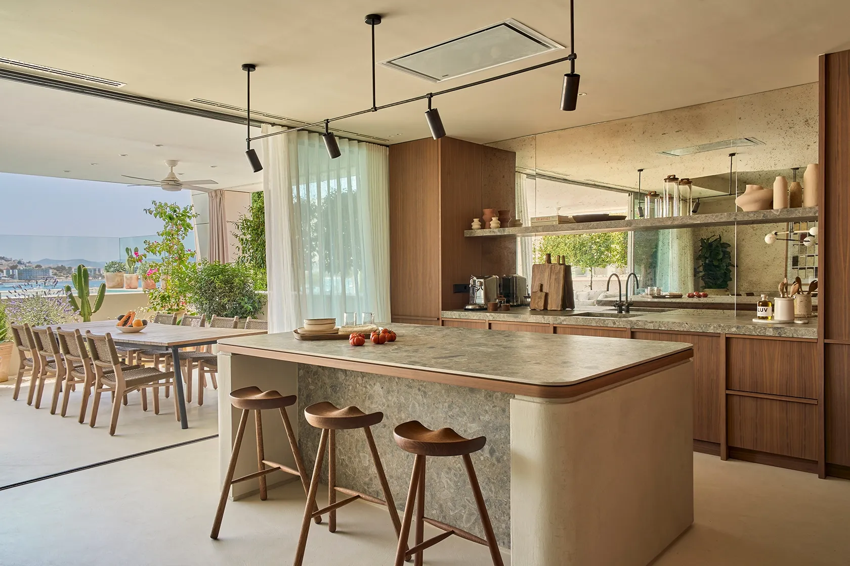 Open kitchen and terrace with stone island, wooden stools, and panoramic sea views in Ibiza residence