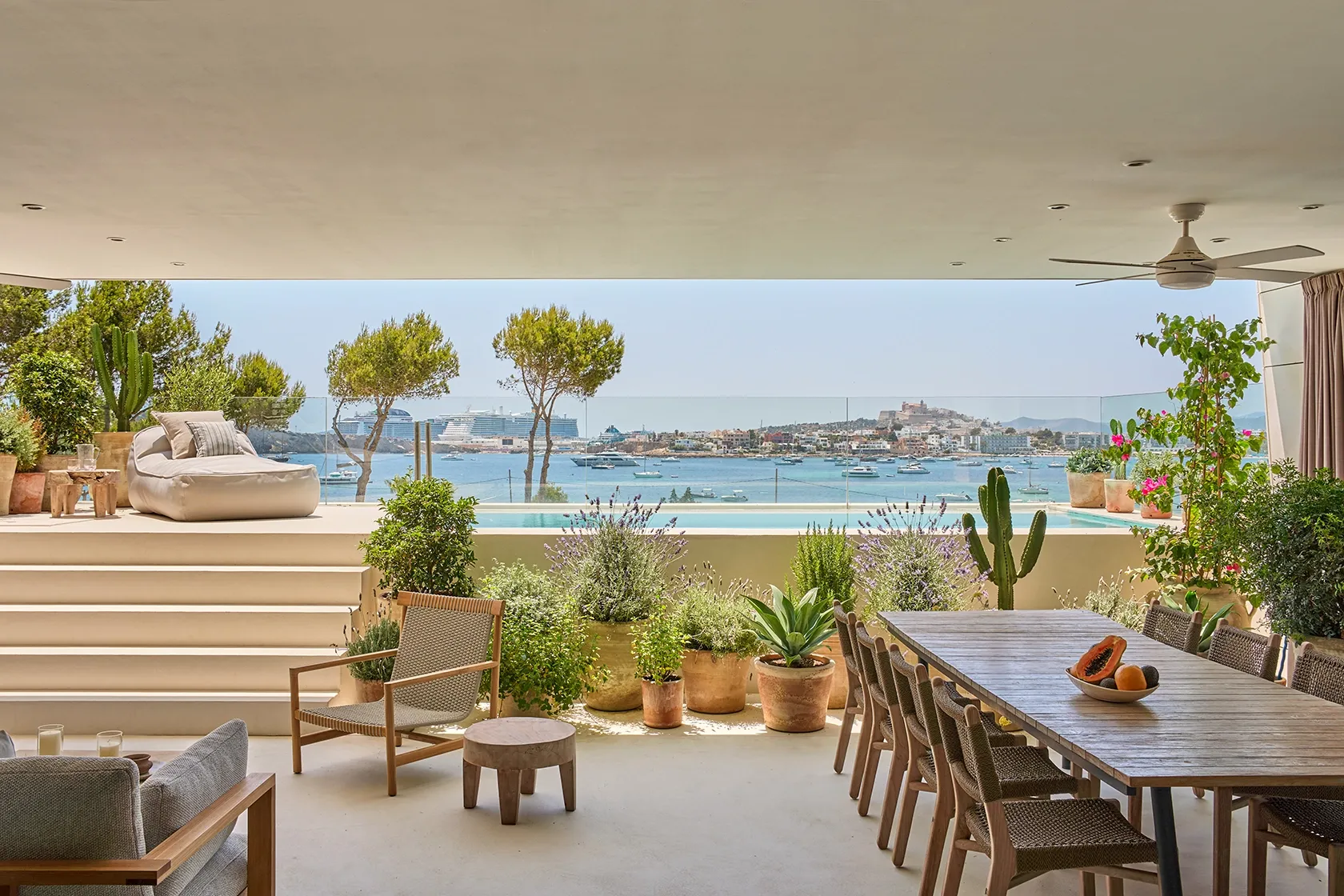 Outdoor terrace with lounge chair, pool, and lush greenery overlooking Ibiza town and sea
