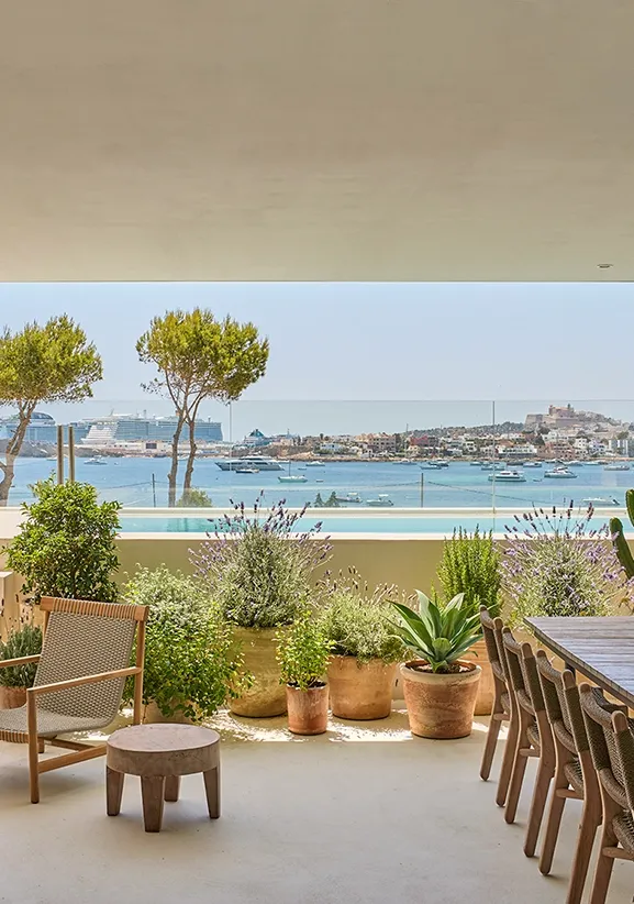 Outdoor terrace with lounge chair, pool, and lush greenery overlooking Ibiza town and sea
