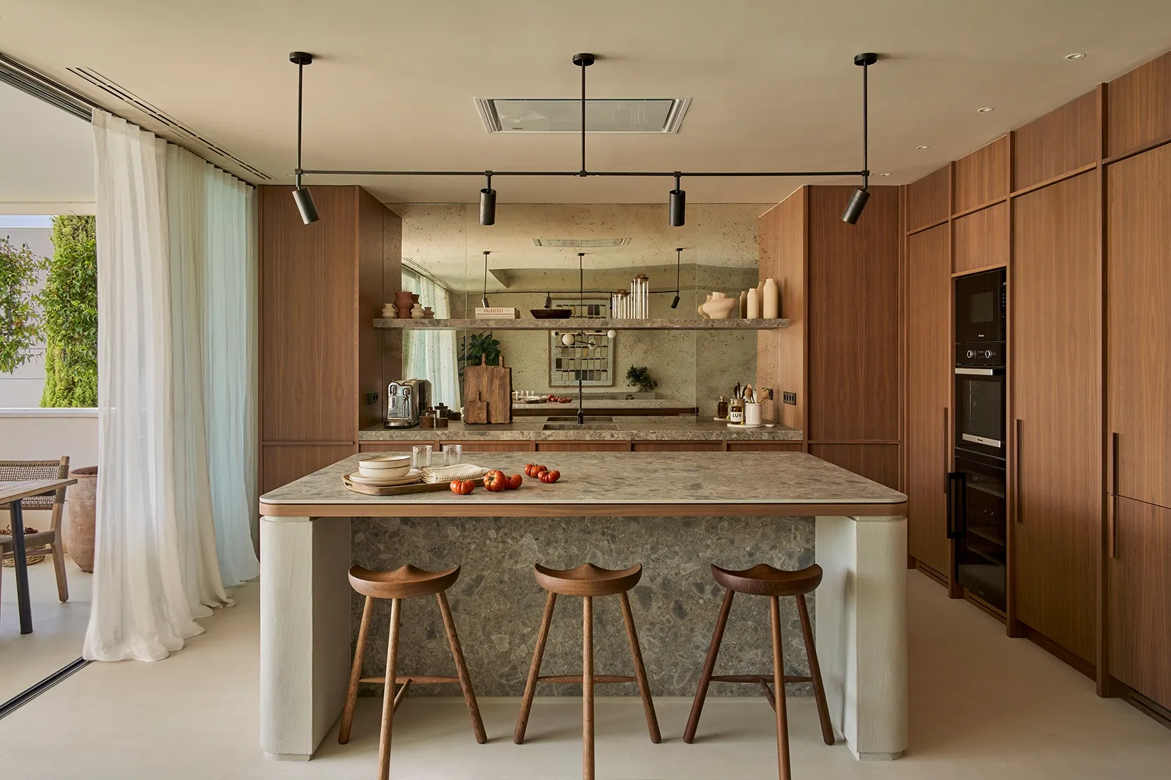 Refined kitchen interior with stone island, minimalist stools, and mirrored backsplash in Ibiza residence