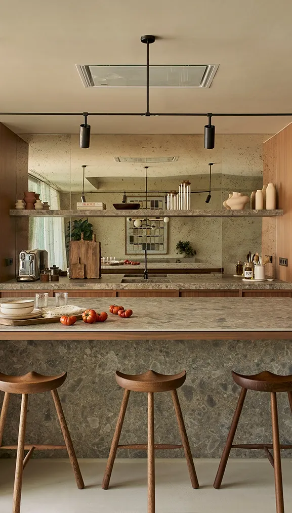 Refined kitchen interior with stone island, minimalist stools, and mirrored backsplash in Ibiza residence