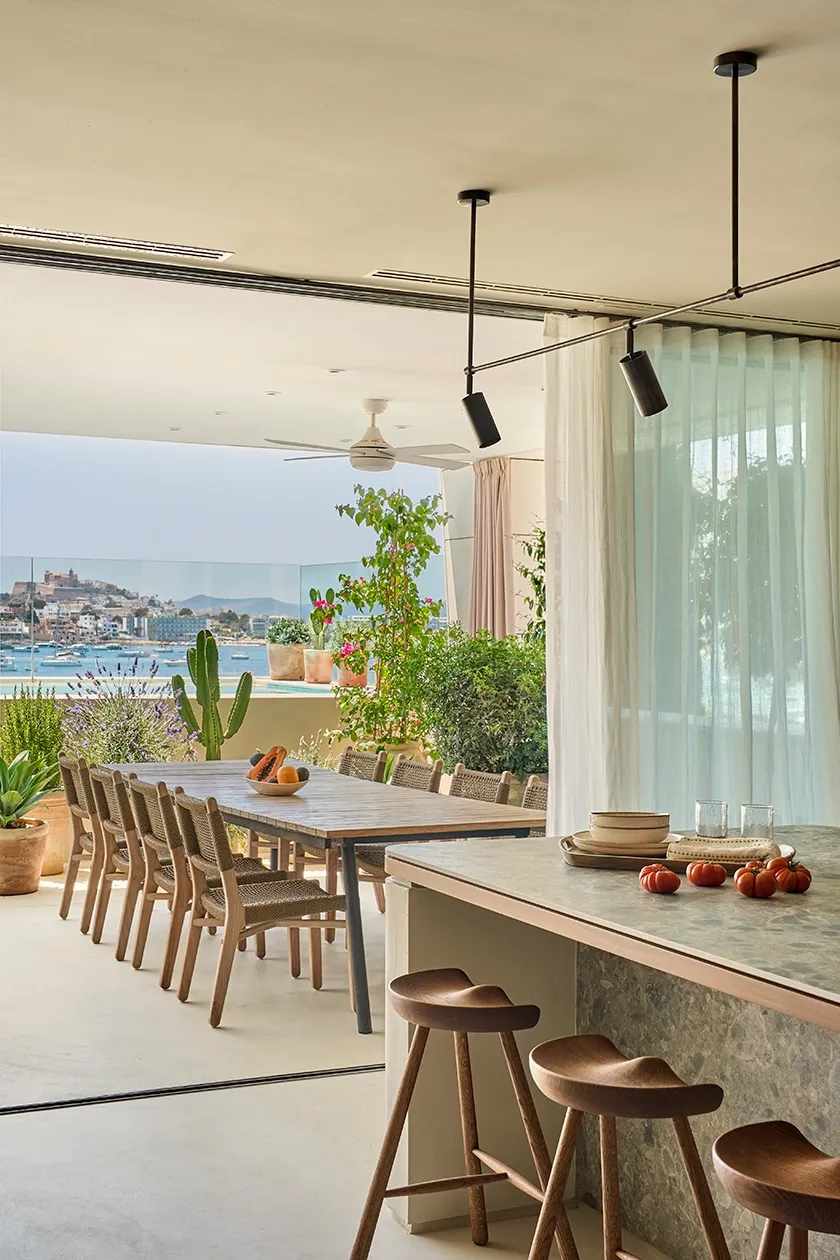 Mediterranean dining terrace with woven chairs, cactus plants, and views of Ibiza port