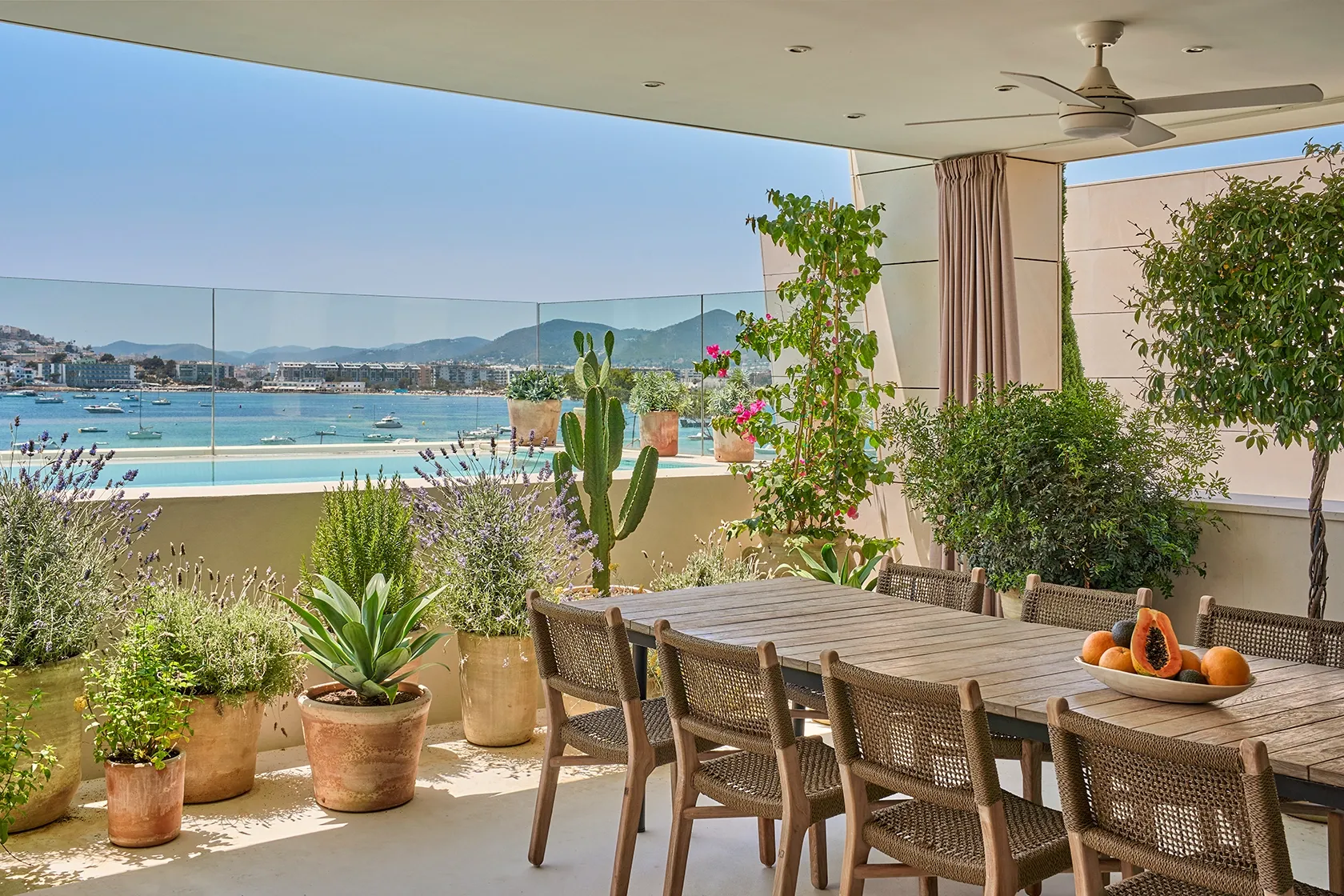 Outdoor terrace with lounge chair, pool, and lush greenery overlooking Ibiza town and sea