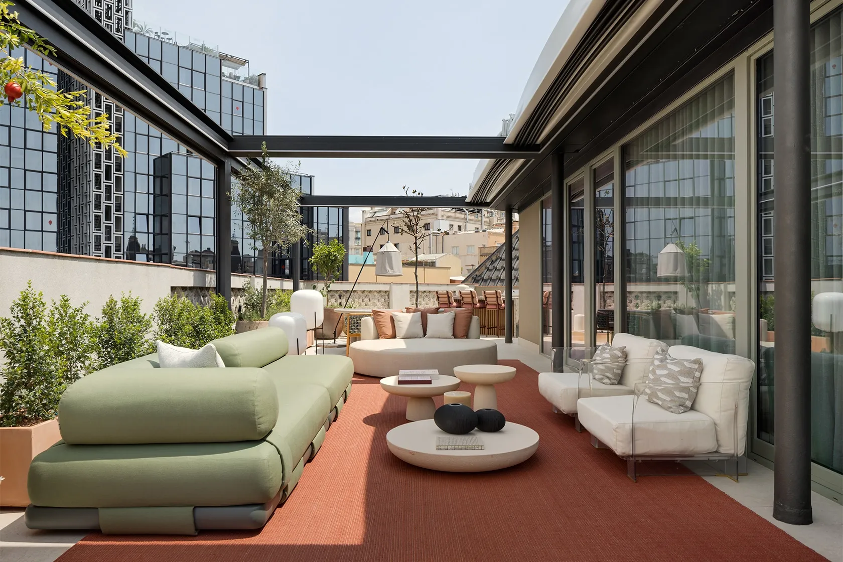 Contemporary rooftop lounge with light grey sofa, terracotta cushions, round ottoman and transparent acrylic armchairs.