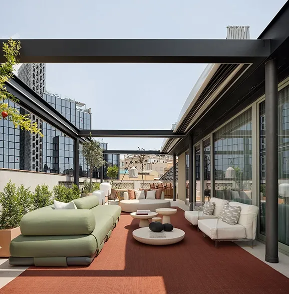 Open rooftop terrace featuring modular green sofa, circular daybed, low stone tables and terracotta outdoor flooring.