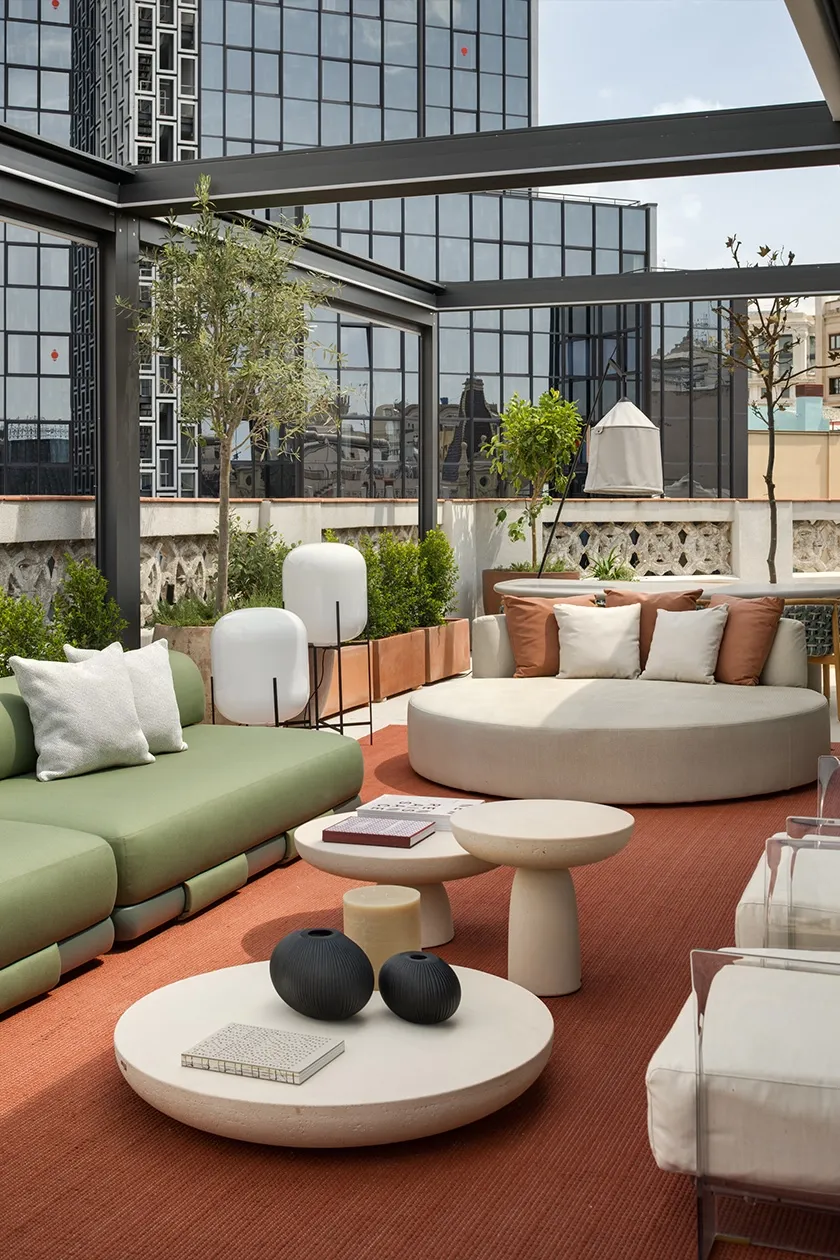 Terrace seating with sage green sofa, round daybed, stone side tables and white opal outdoor floor lamps against urban backdrop.