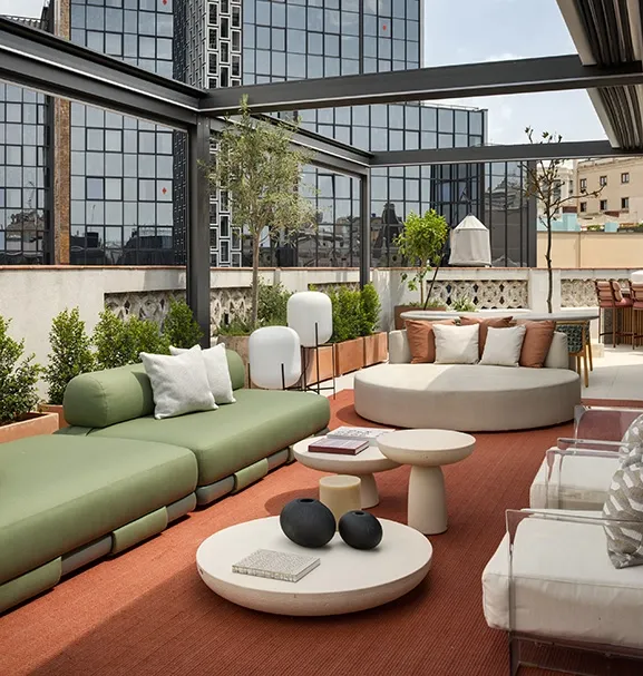 Terrace seating with sage green sofa, round daybed, stone side tables and white opal outdoor floor lamps against urban backdrop.