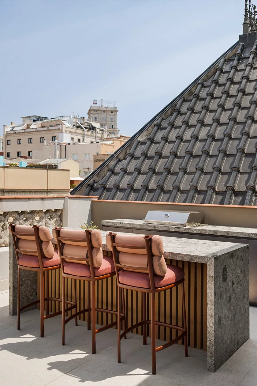 Rooftop bar with grey stone counter, slatted wood detail and terracotta upholstered bar stools overlooking city views.