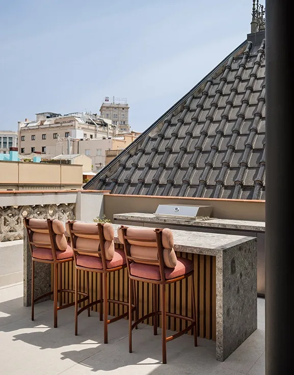 Rooftop bar with grey stone counter, slatted wood detail and terracotta upholstered bar stools overlooking city views.