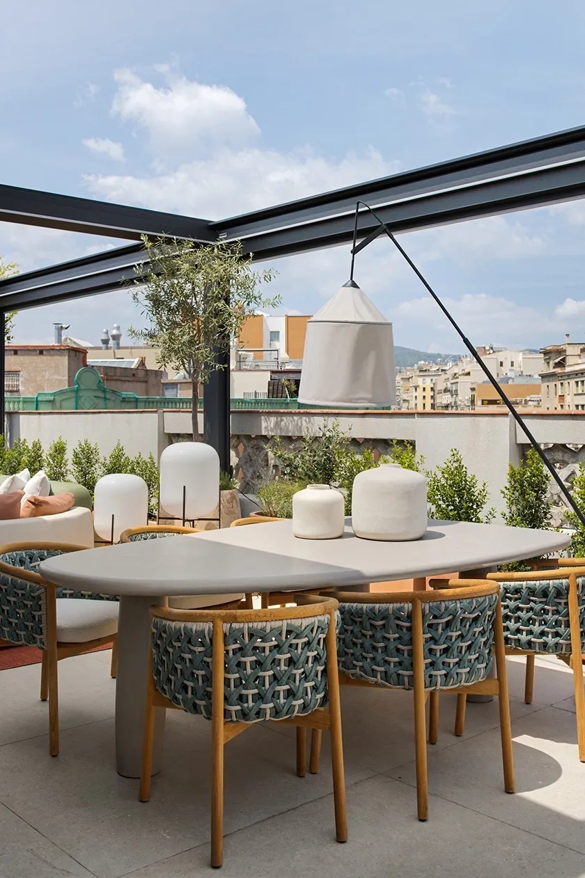 Outdoor dining area with sculptural stone table, woven rope chairs and ceramic decorative vases under pergola structure.