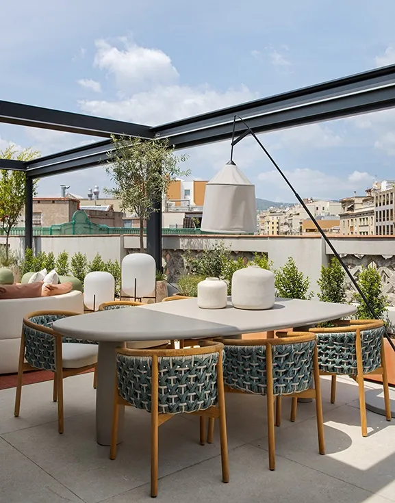 Outdoor dining area with sculptural stone table, woven rope chairs and ceramic decorative vases under pergola structure.