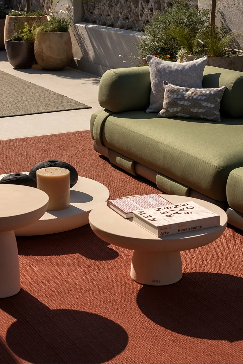 Outdoor lounge with green upholstered sofa, terracotta rug, stone coffee tables and decorative books and vases.
