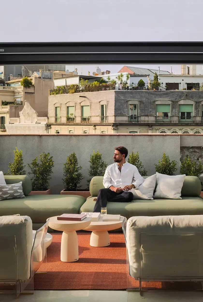 Man sitting on green modular outdoor sofa with stone side tables and city views in the background.