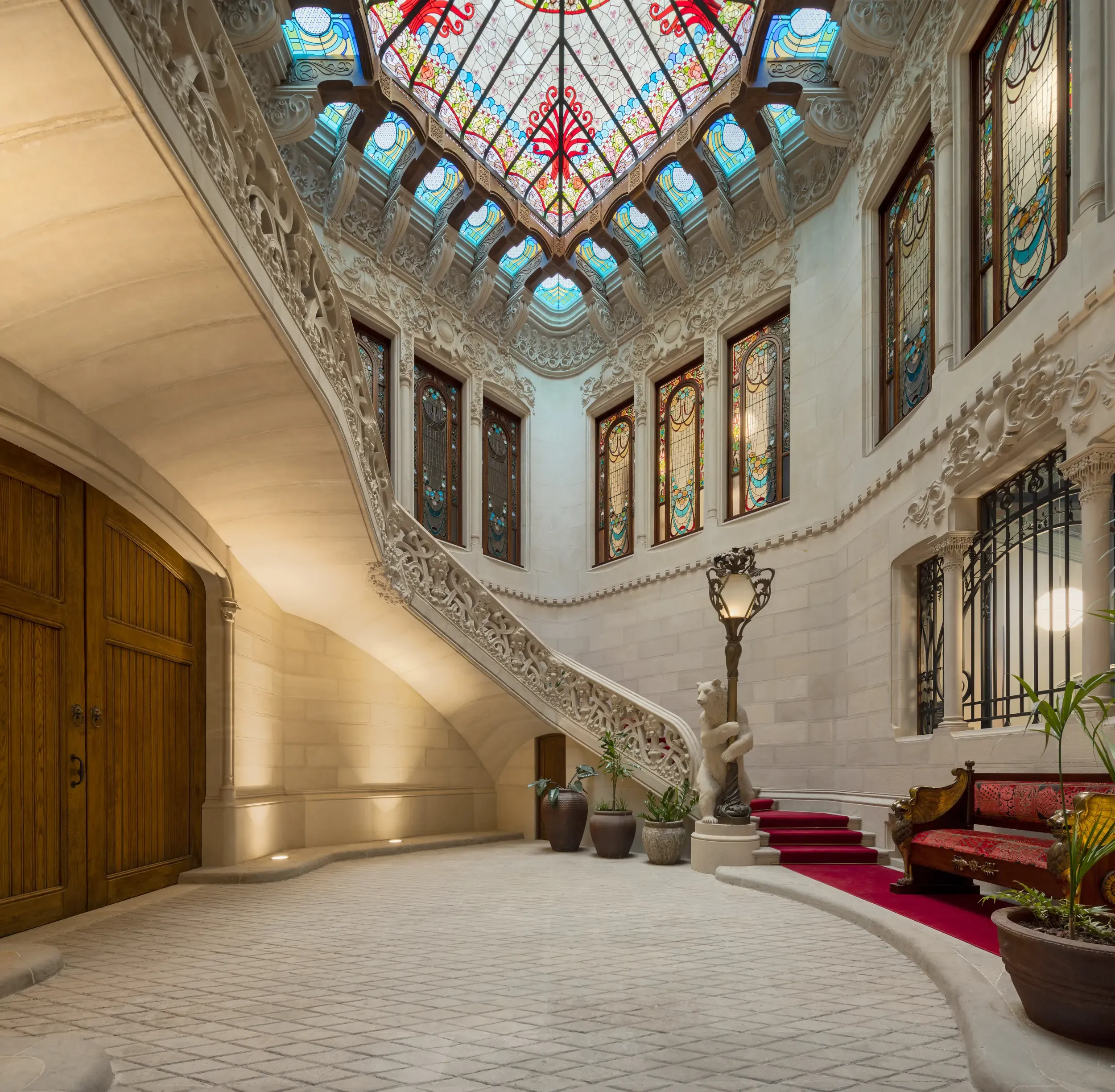 Detail of stained glass ceiling and carved staircase in luxurious historic building interior.