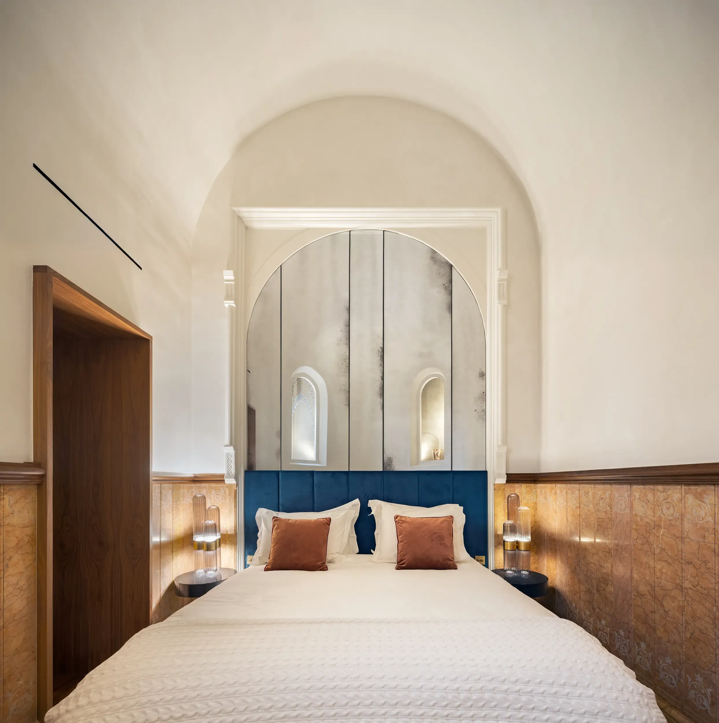 Bedroom with arched ceiling, blue upholstered headboard, and modern lighting blending with historic details.