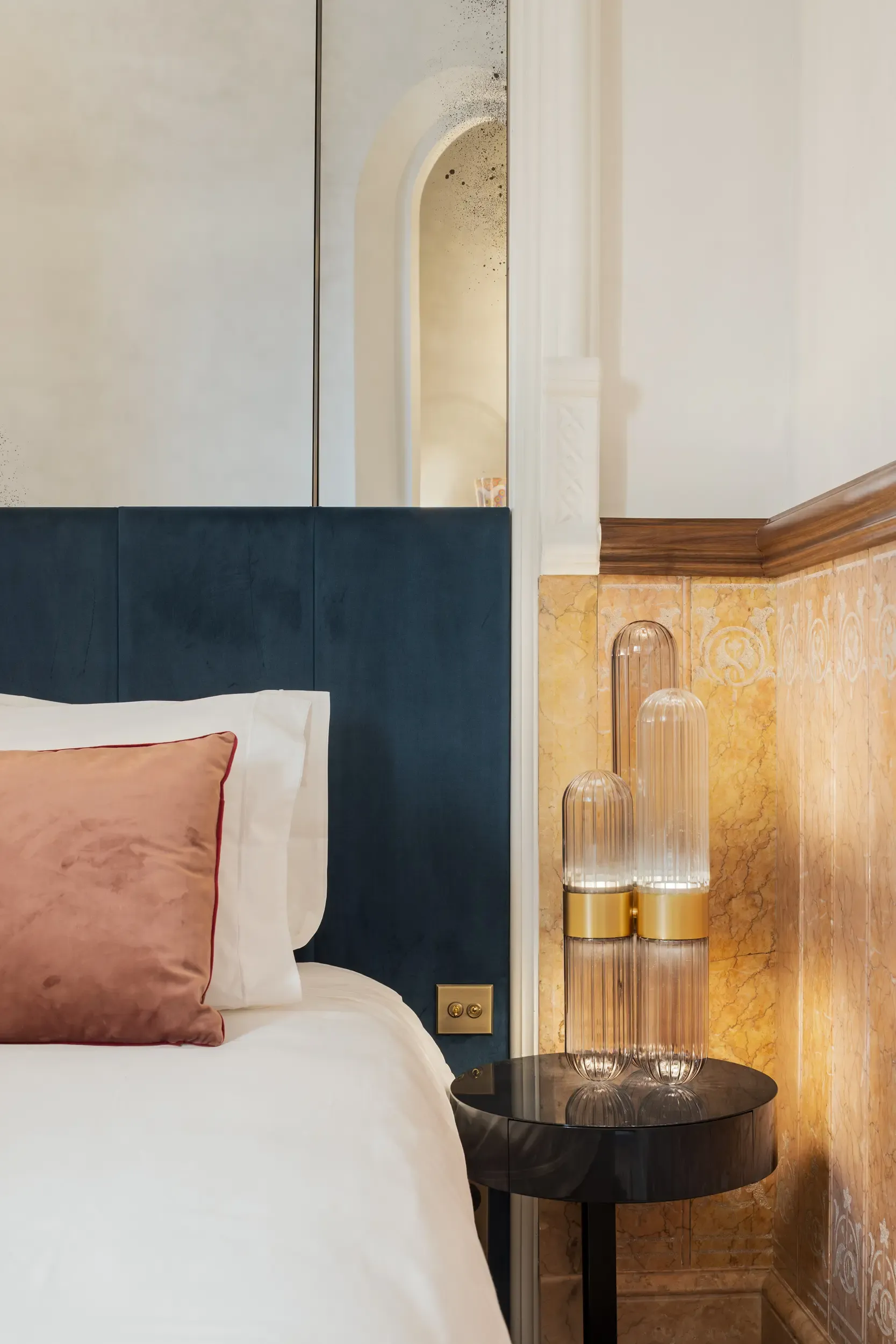 Close-up of bed with velvet cushion, marble walls, and contemporary glass bedside lamps.