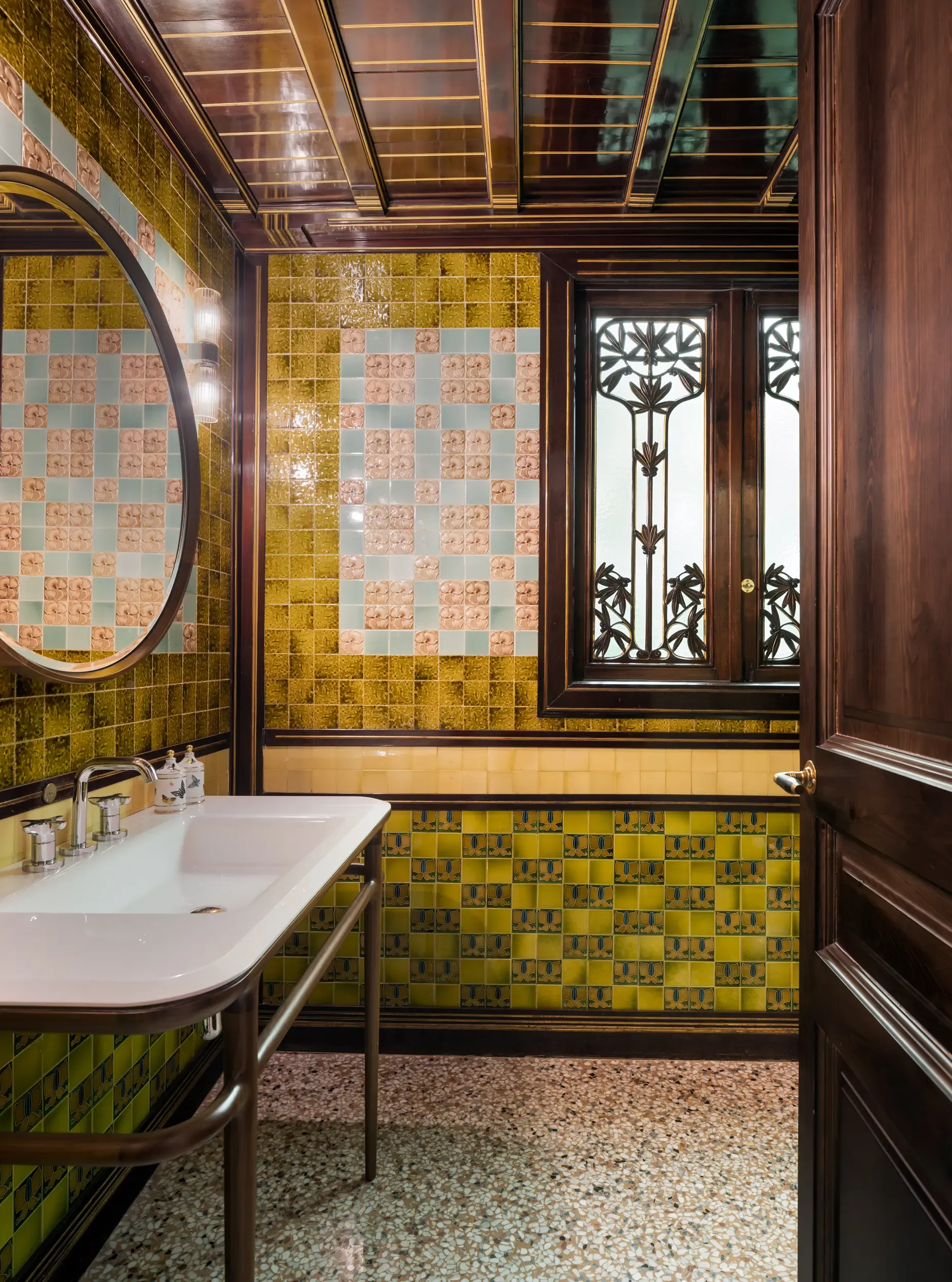 Vintage bathroom with colorful tiled walls, wood finishes, and decorative window grille.