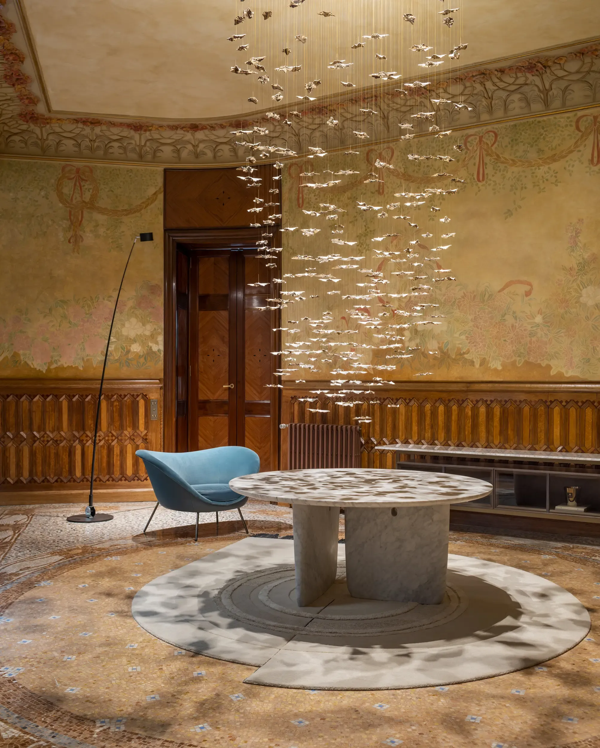 Contemporary art chandelier installation above marble table in ornate historic interior.