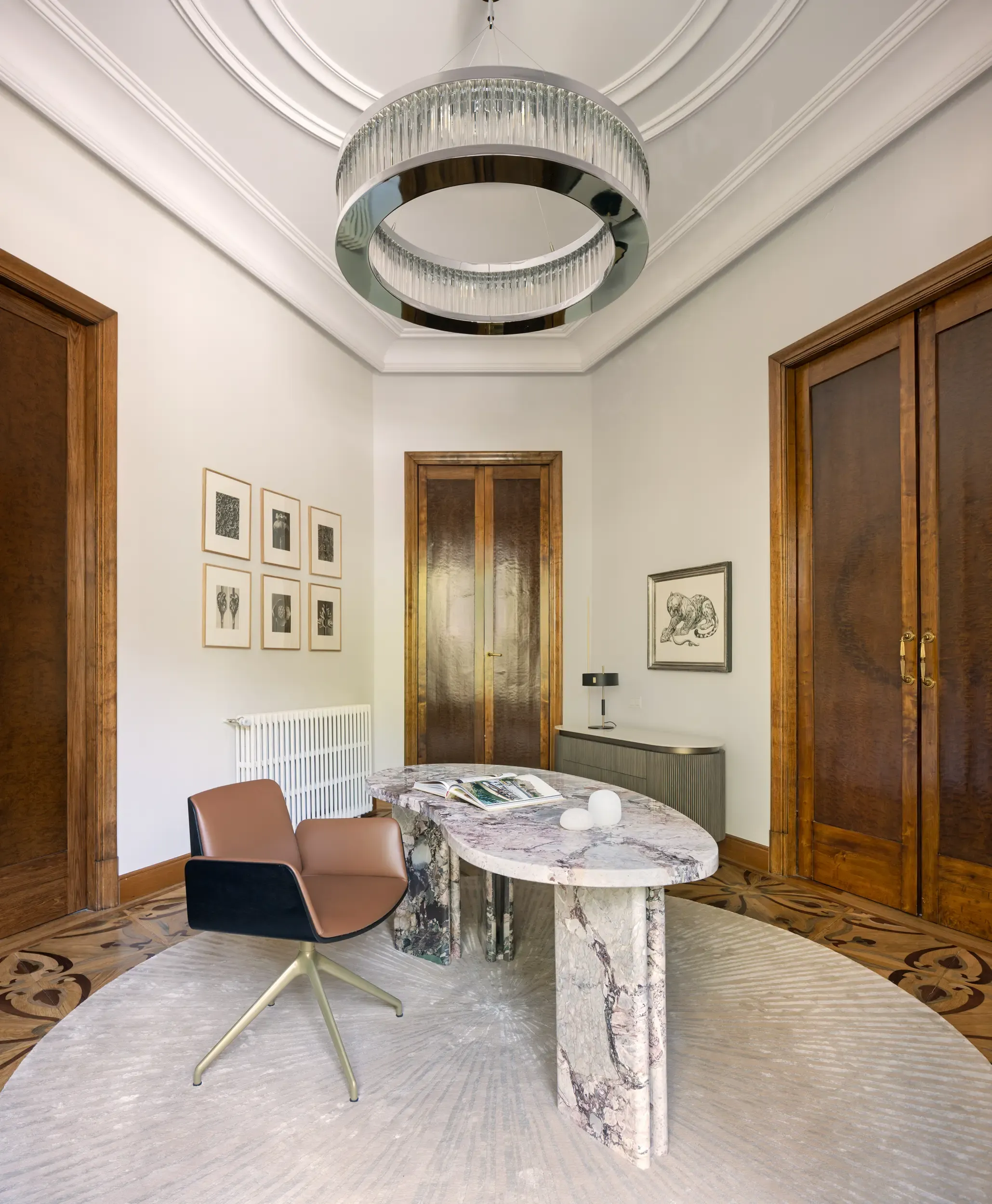Elegant office with marble desk, modern chair, and circular chandelier under classic ceiling details.