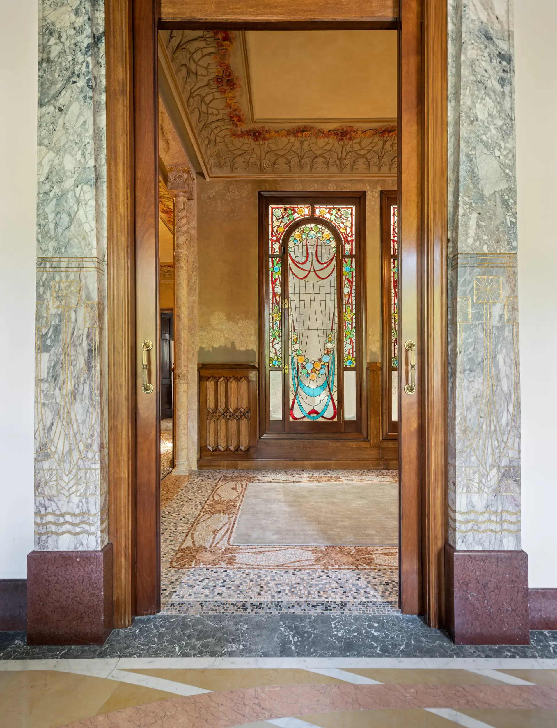 Doorway framed with marble columns opening to stained glass window and decorative wall details.