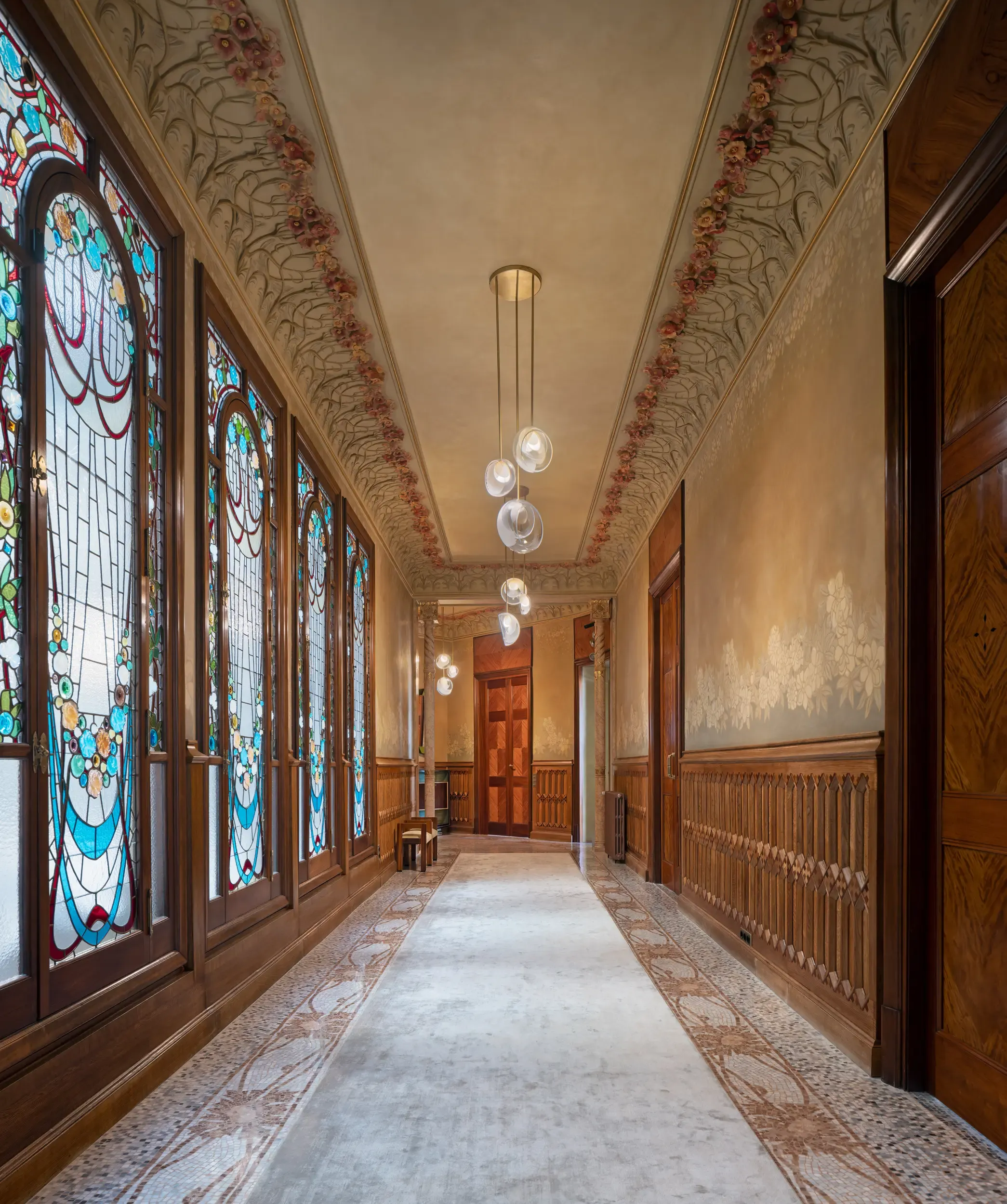 Ornate hallway with stained glass windows, floral ceiling frescoes, and patterned mosaic floor.