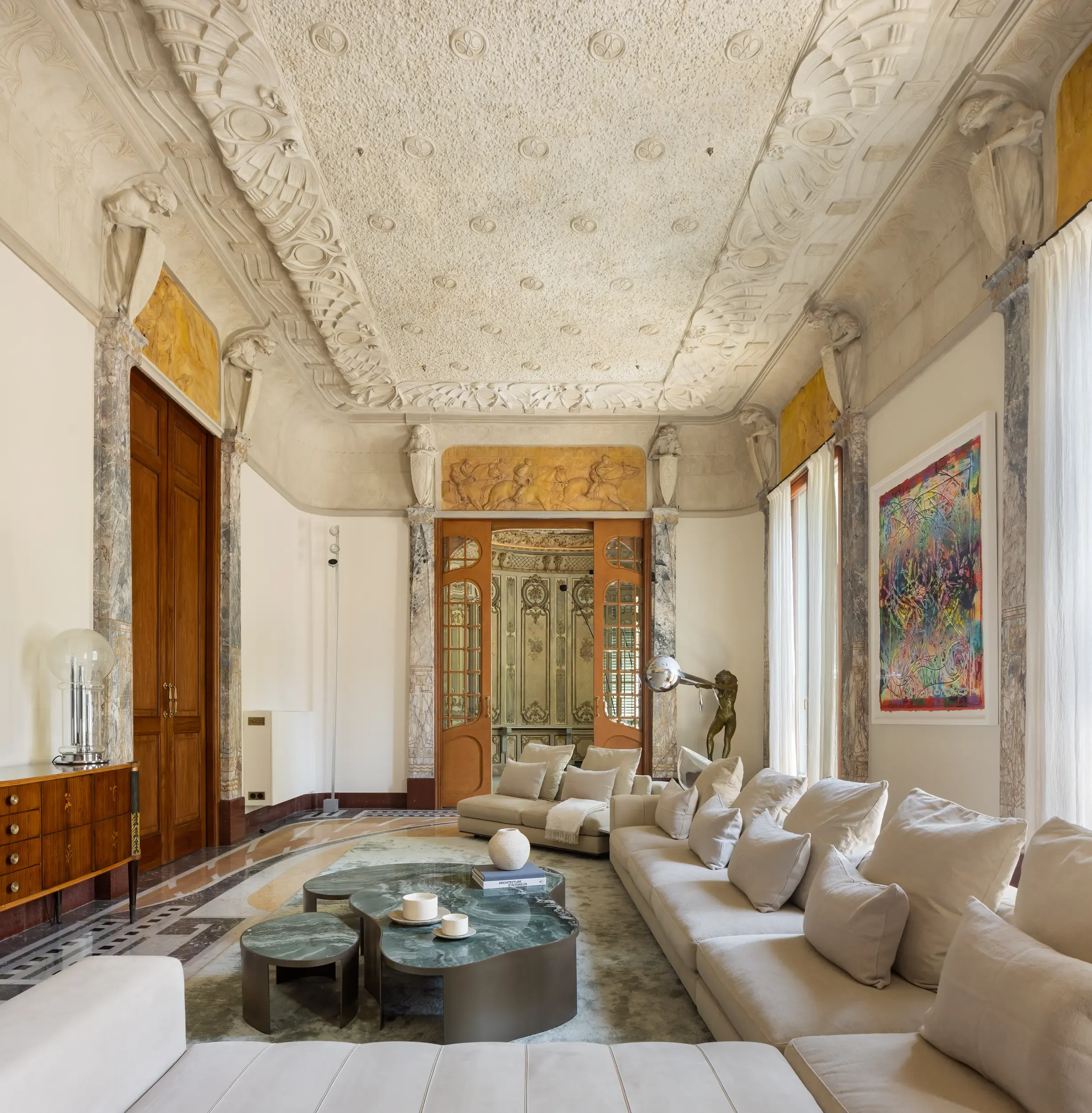 Luxurious living room with sculpted ceiling, large cream sofa, and green marble coffee tables.
