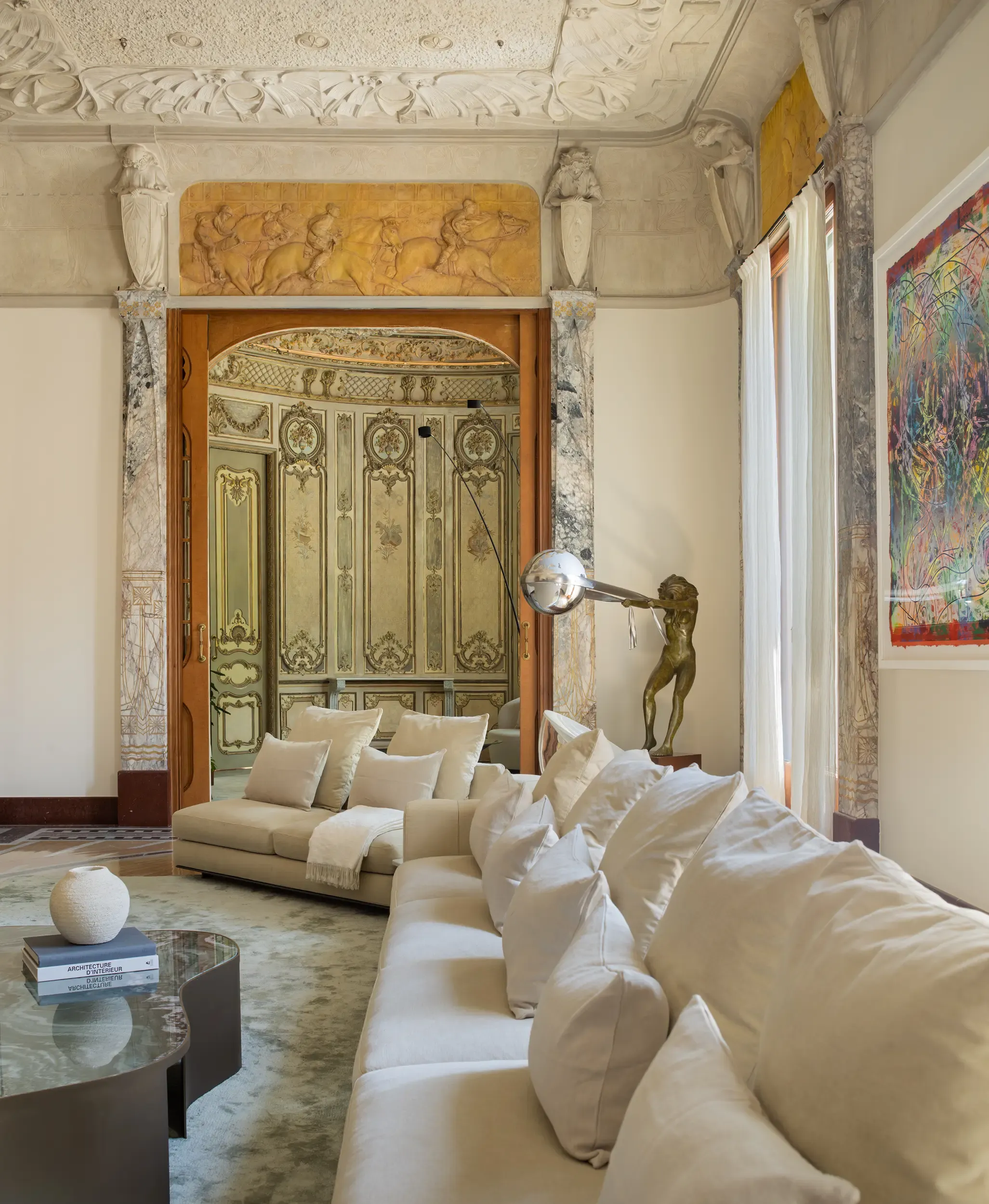 Side view of living room with classical sculptures, ornate doors, and contemporary neutral sofas.