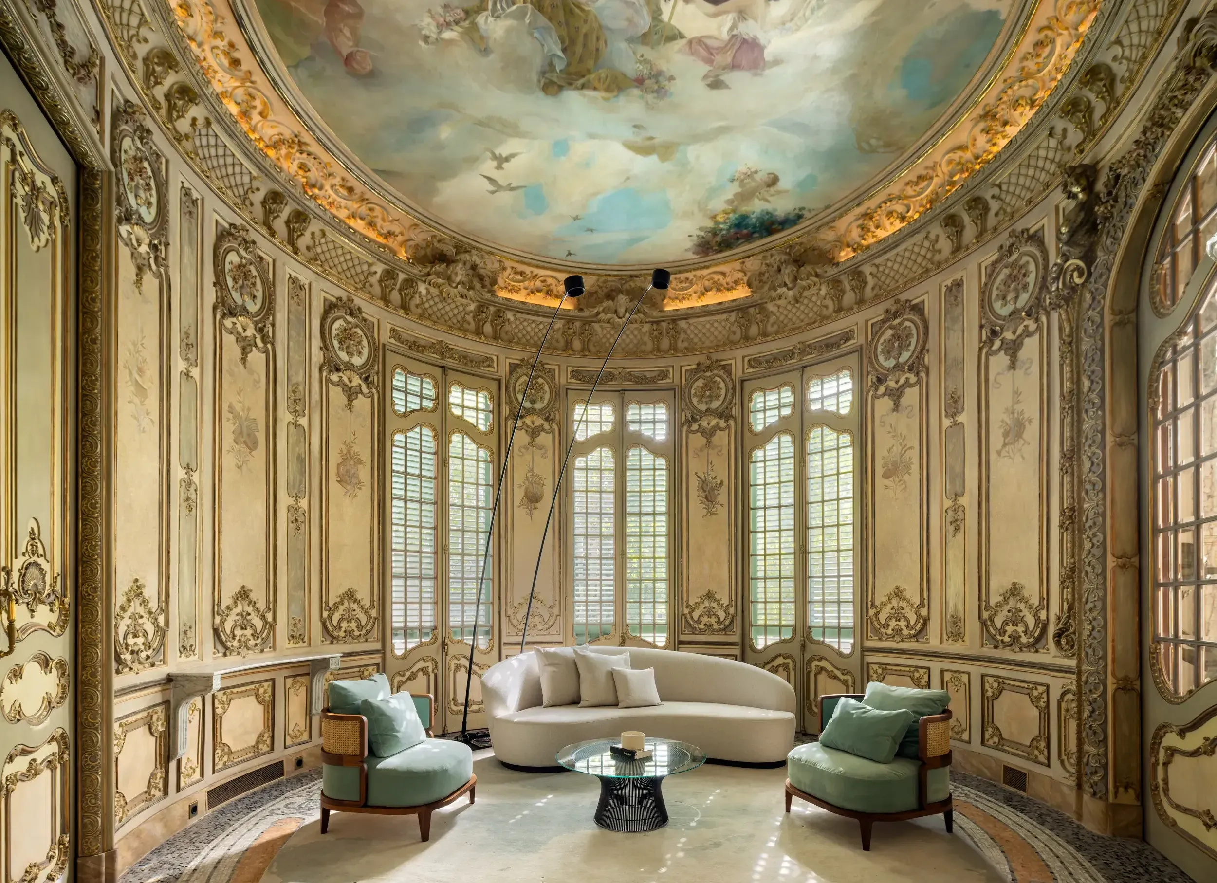 Round lounge with frescoed ceiling, ornate paneling, and curved sofa beneath artistic mural.