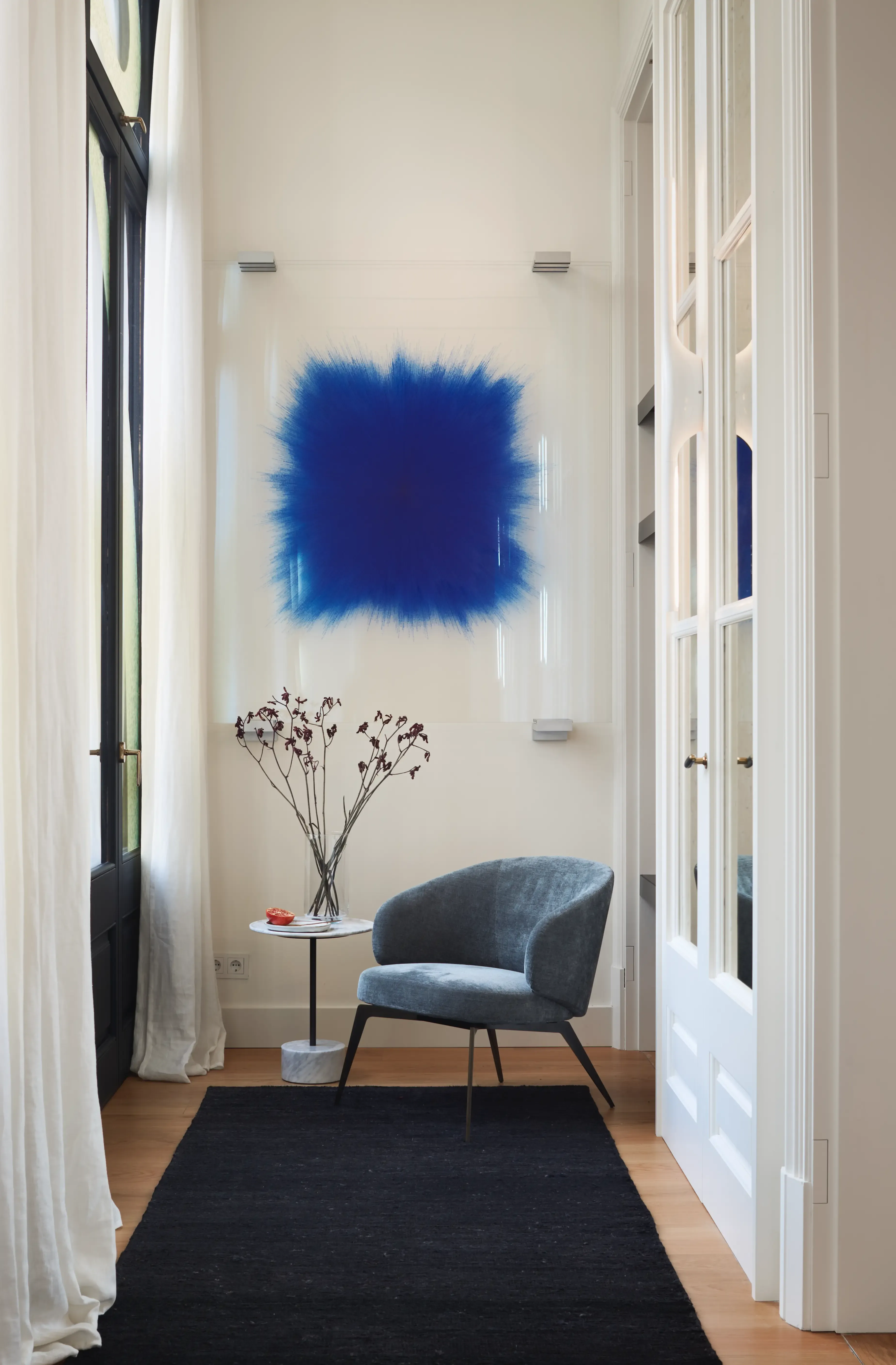 Modern lounge corner with velvet chair, marble side table, and striking blue artwork, emphasizing bold artistic luxury apartment interior.