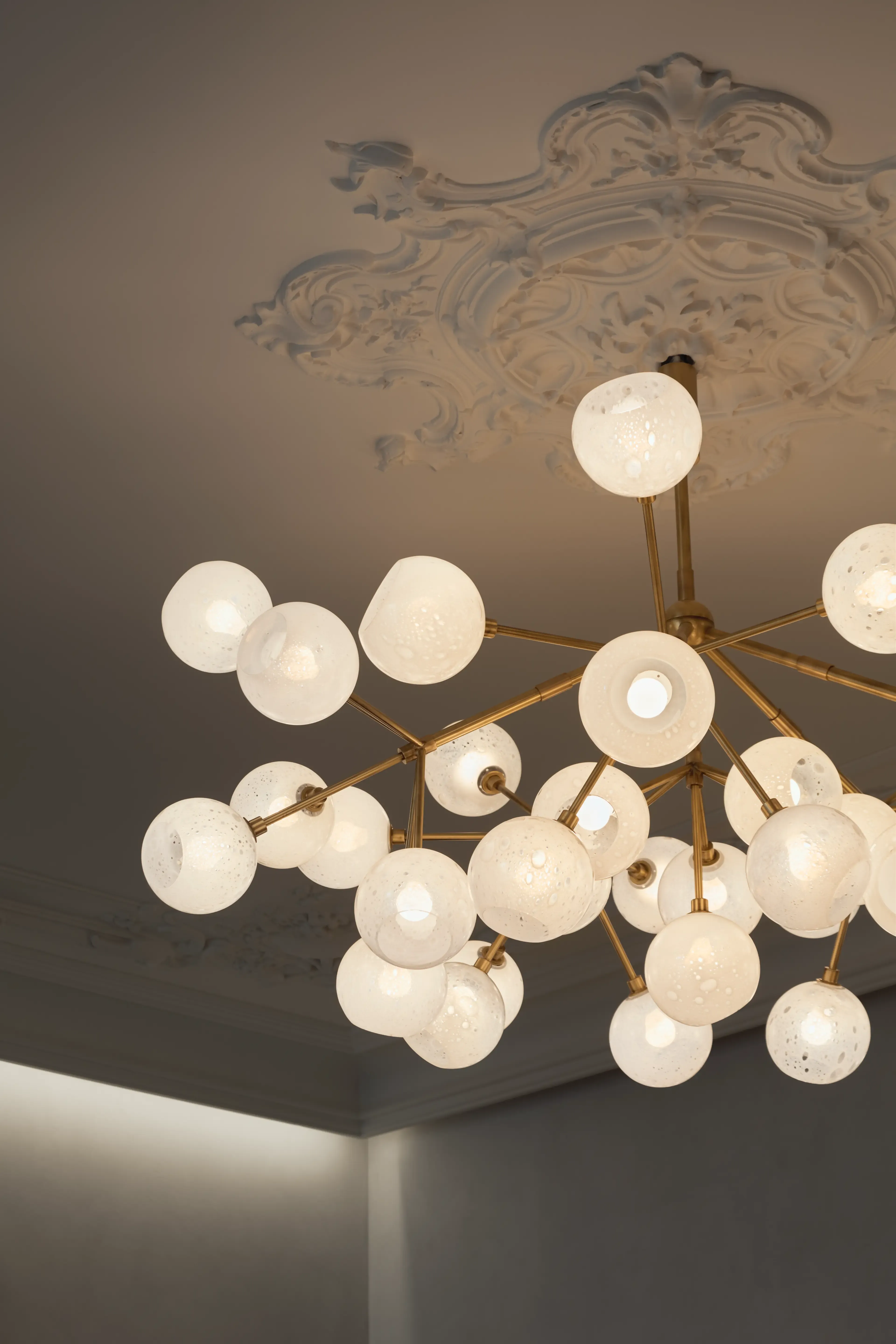 Close-up of designer chandelier with sculptural black shades against ornate ceiling molding, merging modern elegance with classical interior details.