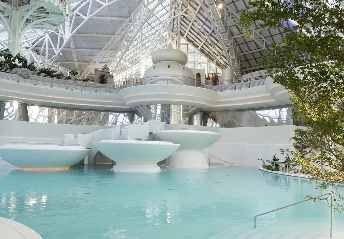 Night view of a dramatic architectural complex with illuminated water pools and angular geometric structures.