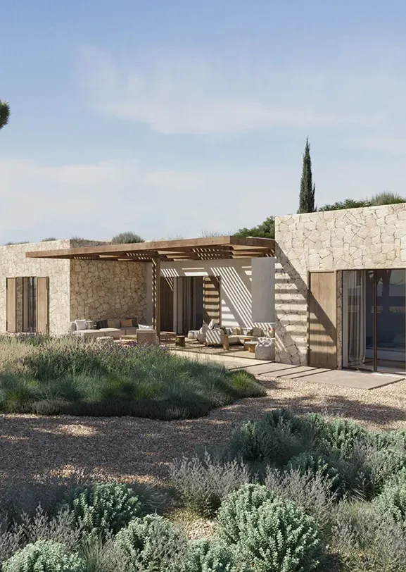 Stone-clad luxury villa nestled in Mediterranean landscape with shaded outdoor lounge area.